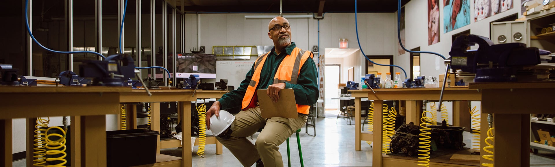 A photo of a man in an orange vest sitting amid a workshop
